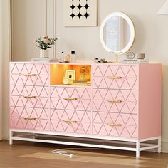 a pink dresser with gold handles and drawers in front of a mirror on the wall