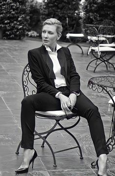 a woman sitting on top of a chair in front of a table with chairs behind her