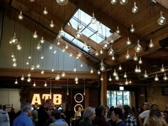 a large group of people standing in a room with many lights hanging from the ceiling