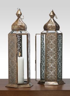 two metal lanterns sitting on top of a wooden table next to each other, one with a candle in it