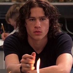 a young man sitting at a table with a lit candle in front of his face