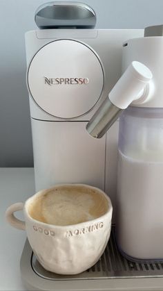 a white coffee maker sitting on top of a counter next to a cup filled with liquid