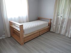 a bed sitting next to a window on top of a hard wood floored floor