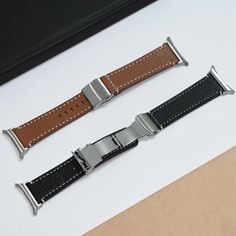 two watches sitting next to each other on top of a white table with brown and black straps