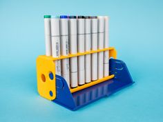 a stack of pens sitting on top of a blue and yellow holder filled with markers