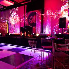 a dance floor is lit up with purple lights and chairs in front of the stage