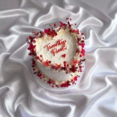 a heart shaped cake with white frosting and red sprinkles