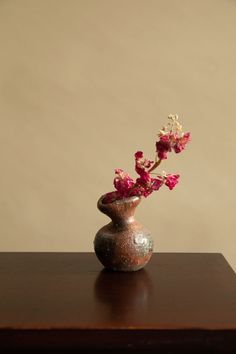 a small vase with flowers in it sitting on a wooden table next to a wall