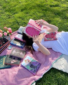 a woman laying on top of a pink blanket with lots of books and magazines next to her