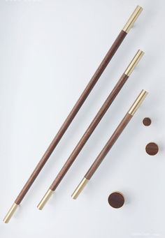 three wooden chopsticks with gold colored tips and two brown ones on a white surface