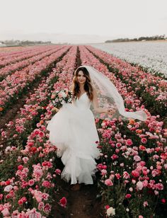 a woman in a white wedding dress standing in a field with lots of pink flowers