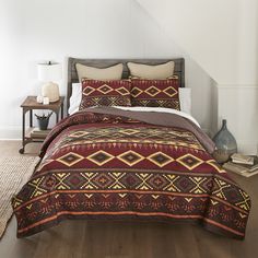 a bed with a red and yellow comforter on top of it in a bedroom