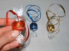 a hand is holding an ornament with ribbon around it and three other ornaments in the background