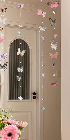 a vase filled with pink flowers next to a white door and butterflies hanging from the ceiling