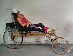 a woman sitting on top of a bike next to a white brick wall and wearing a helmet