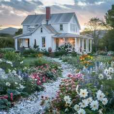 a white house with lots of flowers in the front yard and walkway leading to it