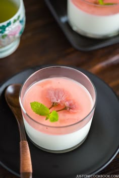 a small glass filled with watermelon on top of a black plate next to a spoon