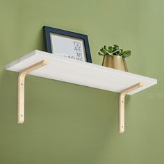 a white shelf with a potted plant next to it and a framed print on the wall