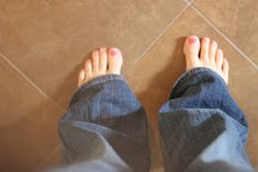 a person's feet with pink nail polish standing on a tile floor