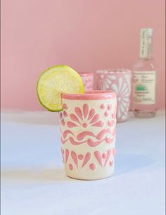 a pink and white cup with a lime slice in it sitting on a table next to bottles