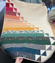 a woman is holding up a quilt made from strips of fabric