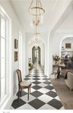 an elegant hallway with black and white checkered flooring, chandelier and chairs