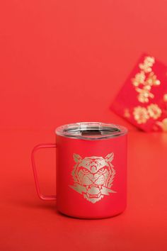 a red coffee mug with a gold tiger on the side and a red box in the background