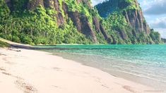 a sandy beach with blue water and mountains in the background