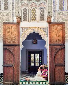 two women sitting on the ground in front of an ornate doorway with colorful tiles and wooden doors