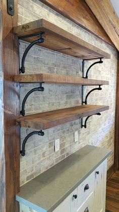 three wooden shelves with metal brackets against a brick wall