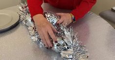 a woman in red shirt decorating silver tinsel wreaths on top of a table