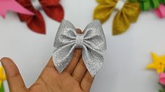 a hand holding a small silver bow on it's finger in front of colorful paper flowers