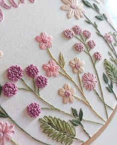 a close up of a embroidery pattern on a white surface with pink flowers and green leaves