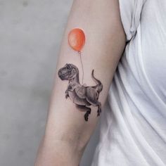 a woman's arm with a dinosaur tattoo on it and an orange balloon in the shape of a t - rex