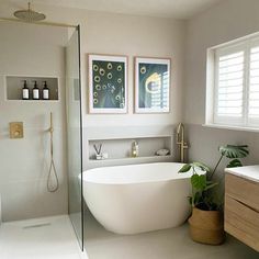 a white bath tub sitting in a bathroom next to a sink and shower with two framed pictures on the wall