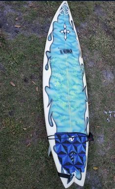 a surfboard with blue and white designs on it laying in the grass next to some rocks