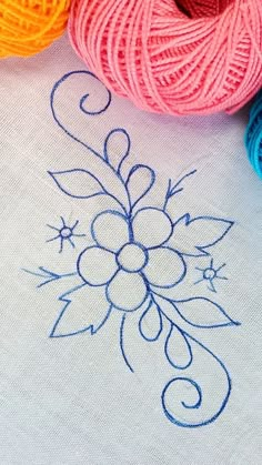 some balls of yarn are sitting next to each other on a white tablecloth with blue and yellow stitching