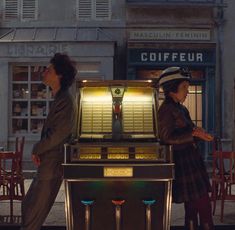 two people standing in front of a machine that is on the street next to each other