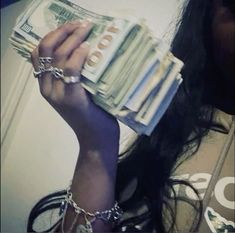 a woman is holding money in her hand and wearing chain around her neck while she's looking at the camera