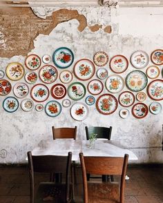 plates are arranged on the wall above two dining room tables with chairs in front of them