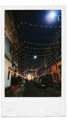 an empty street with lights strung over it and cars parked on the side of the road