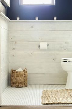 a white toilet sitting under a window next to a rug on top of a wooden floor