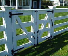 a white fence with black hardware on the top and bottom bars is in front of a house