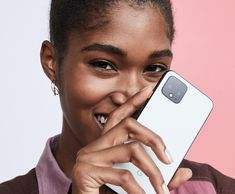 a woman holding up a cell phone to her face and smiling at the camera with both hands