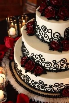 a three tiered wedding cake with red roses on the side and candles behind it