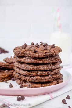 a stack of chocolate cookies on a plate next to a glass of milk and strawberries