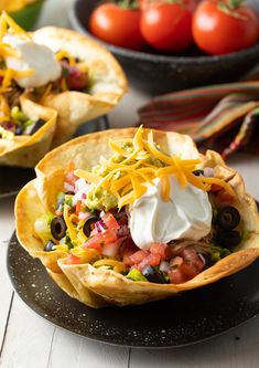 two tacos filled with various toppings on top of a black plate next to tomatoes