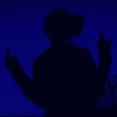 the silhouette of a person holding a cell phone in their hand, against a dark blue background