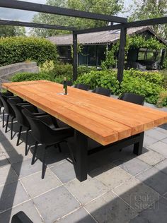 an outdoor dining table with black chairs and a bottle of wine on the table in front of it