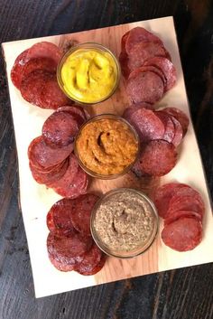 several different types of meats on a cutting board with dips and sauces